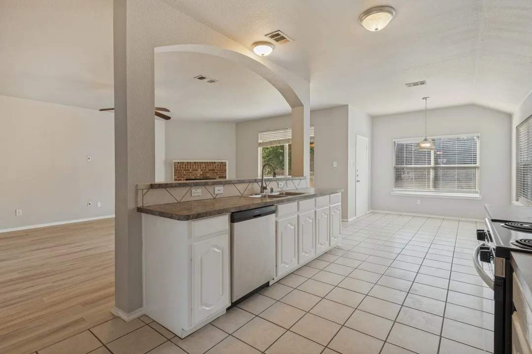 Kitchen featuring white cabinetry, a built-in dishwasher, tile flooring, and a window with blinds