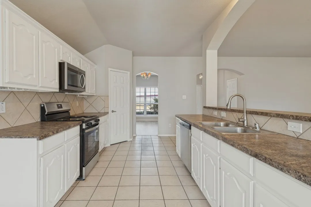 White cabinetry, stainless steel appliances, dual basin sink, patterned tile backsplash, and light tile flooring