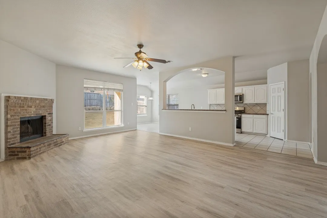 Spacious living area featuring wood-finish flooring, a brick fireplace, and vaulted ceilings