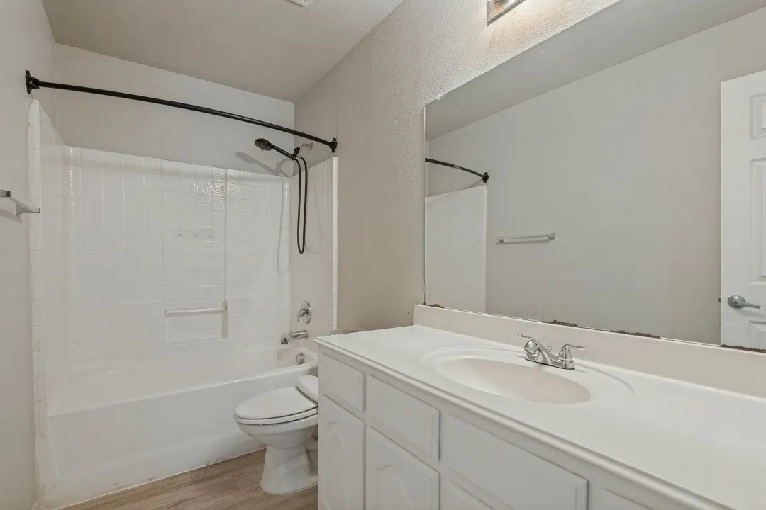 Bathroom featuring a shower-tub combination with white subway tile surround, single vanity with integrated sink, and wood-finish flooring