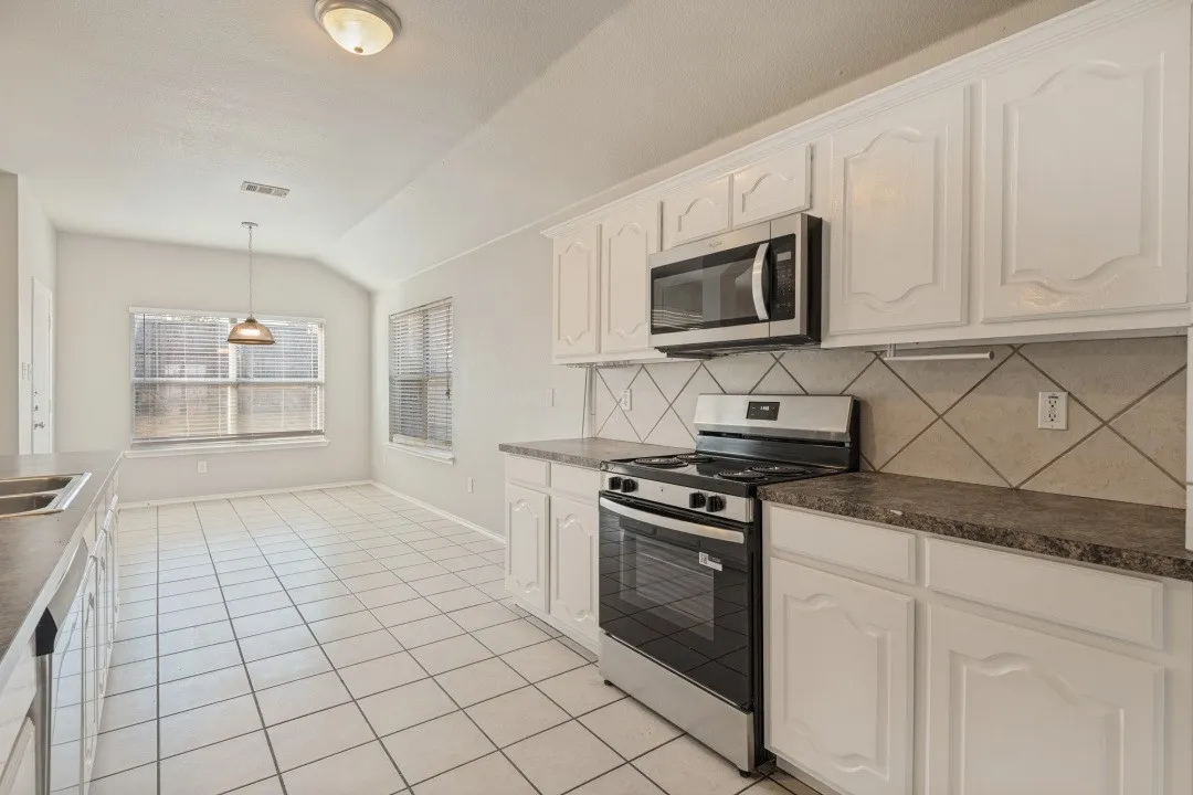White cabinetry, stainless steel range, stainless steel microwave, large windows, and tile flooring