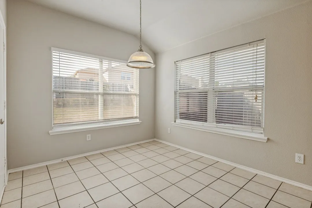 Vaulted ceiling, tiled flooring, two large windows with blinds, and an overhead pendant light fixture
