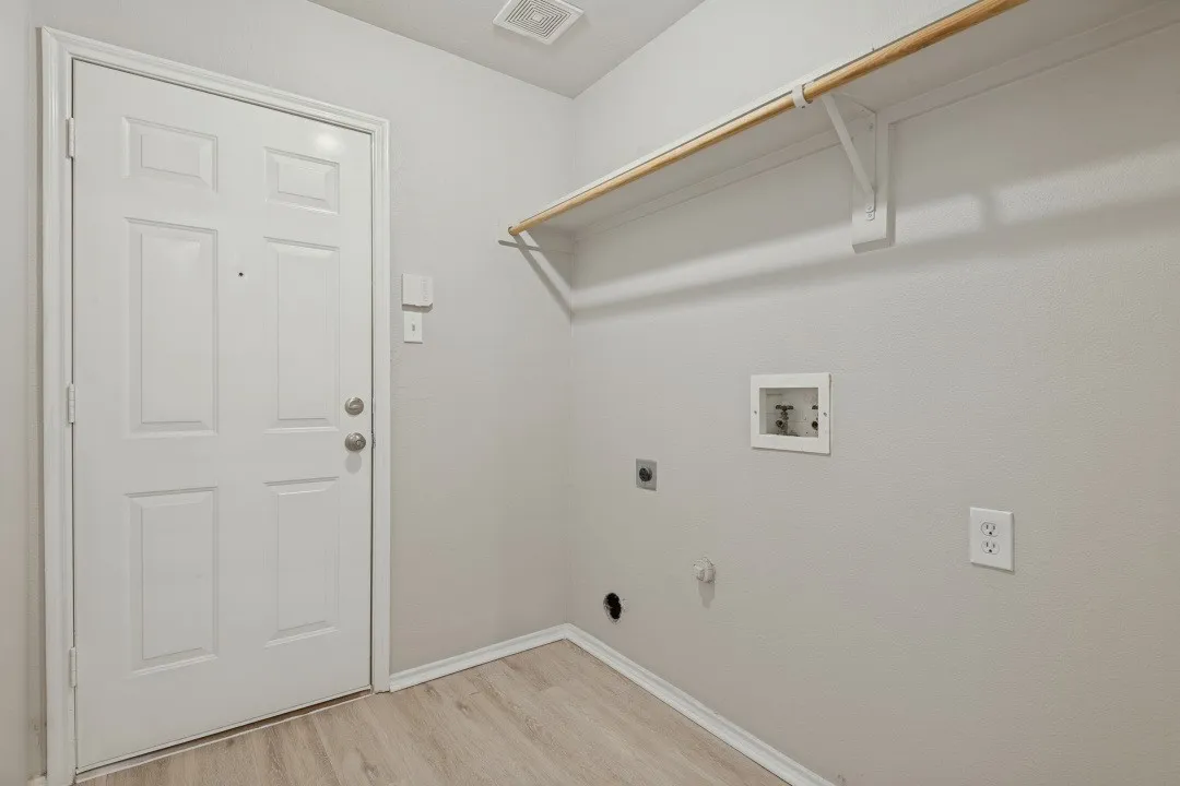 Wood-finish flooring, laundry connections, white paneled door, and overhead rod