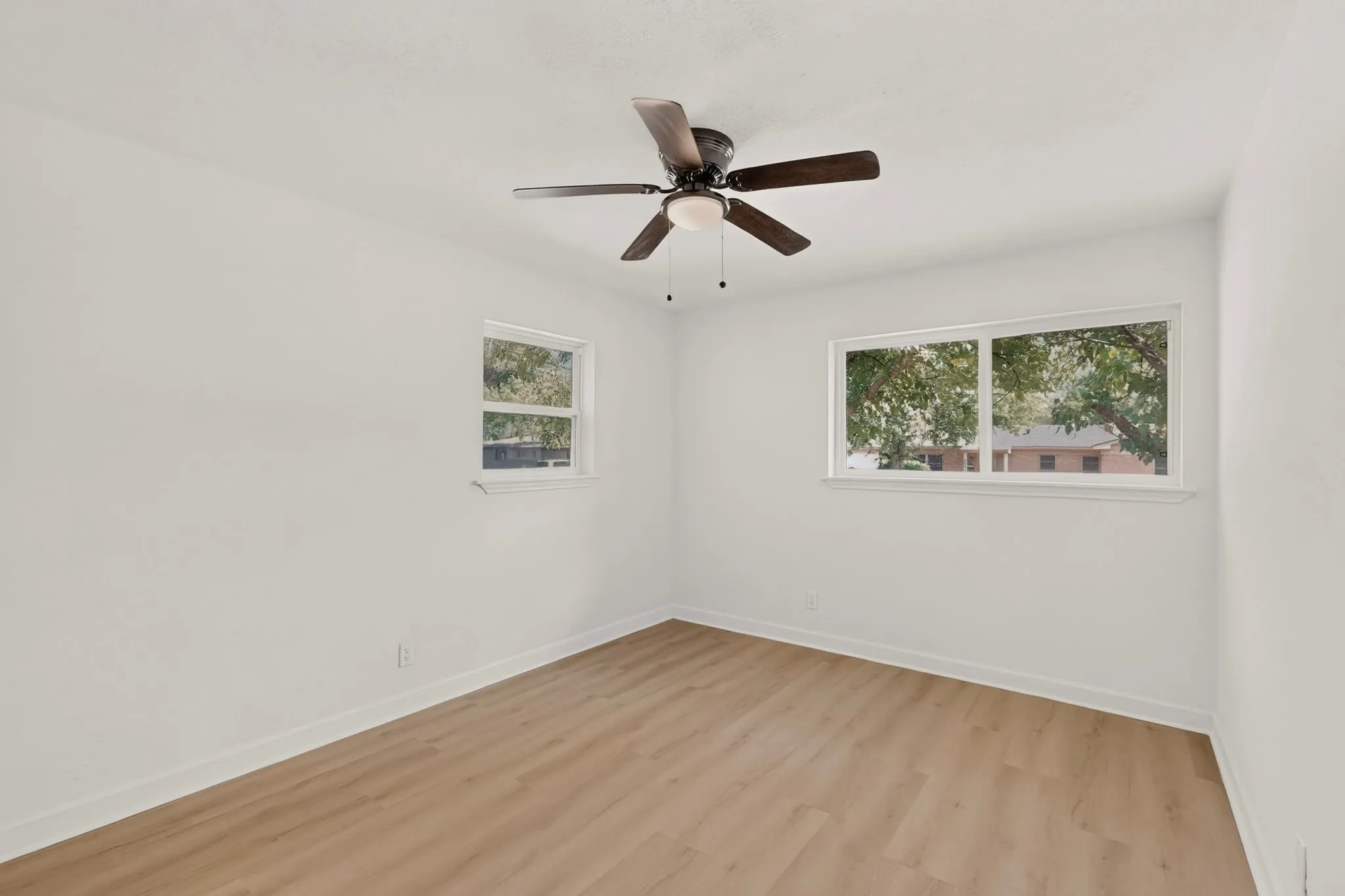 Wood-finish flooring, white walls, and a ceiling fan with integrated lighting