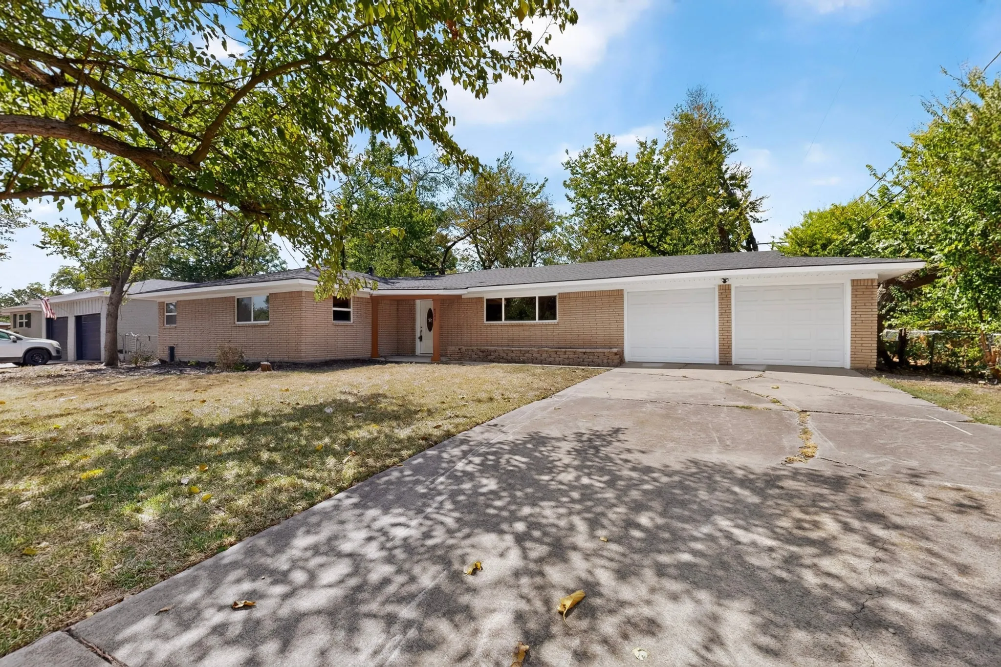Brick exterior, attached two-car garage, concrete driveway, and a front lawn with mature trees