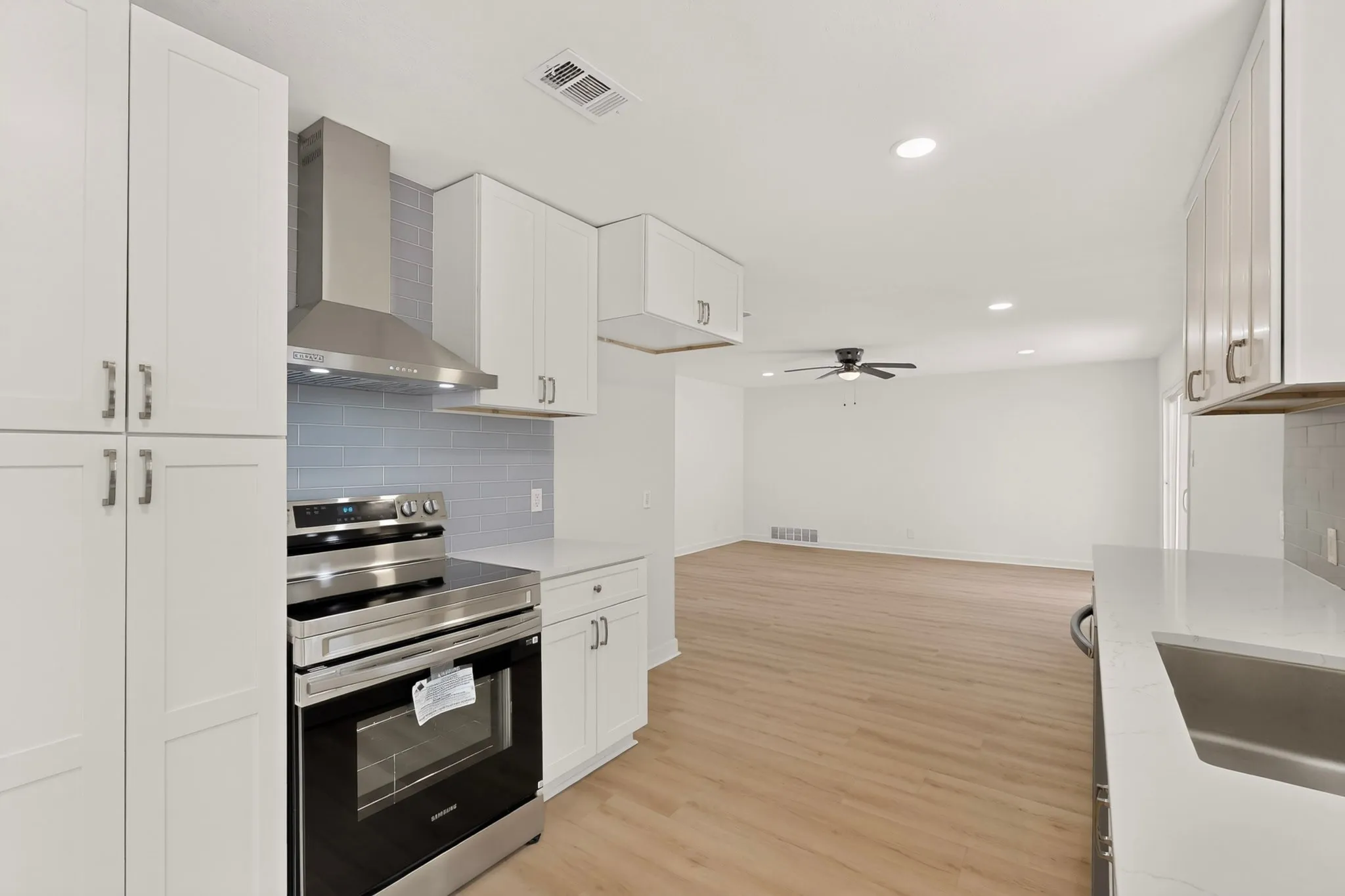 Modern kitchen featuring white shaker cabinetry, stainless steel range with matching hood, subway tile backsplash, and light-toned wood-finish flooring