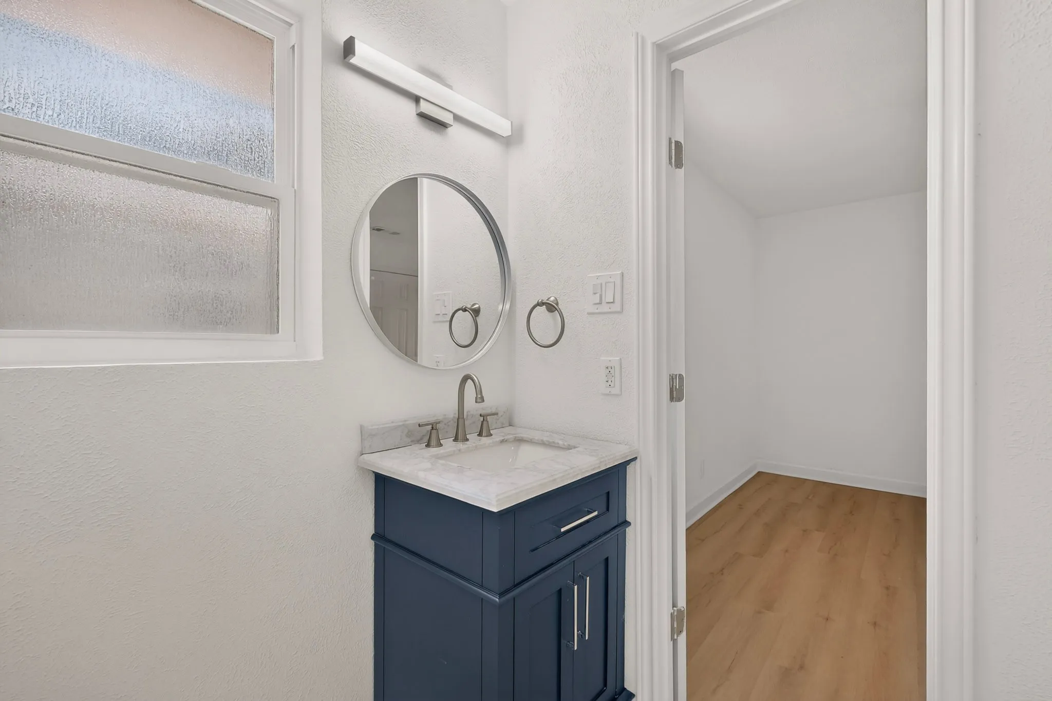 Frosted window providing privacy, modern vanity with blue cabinetry, integrated sink, and brushed nickel faucet, illuminated by an overhead light fixture