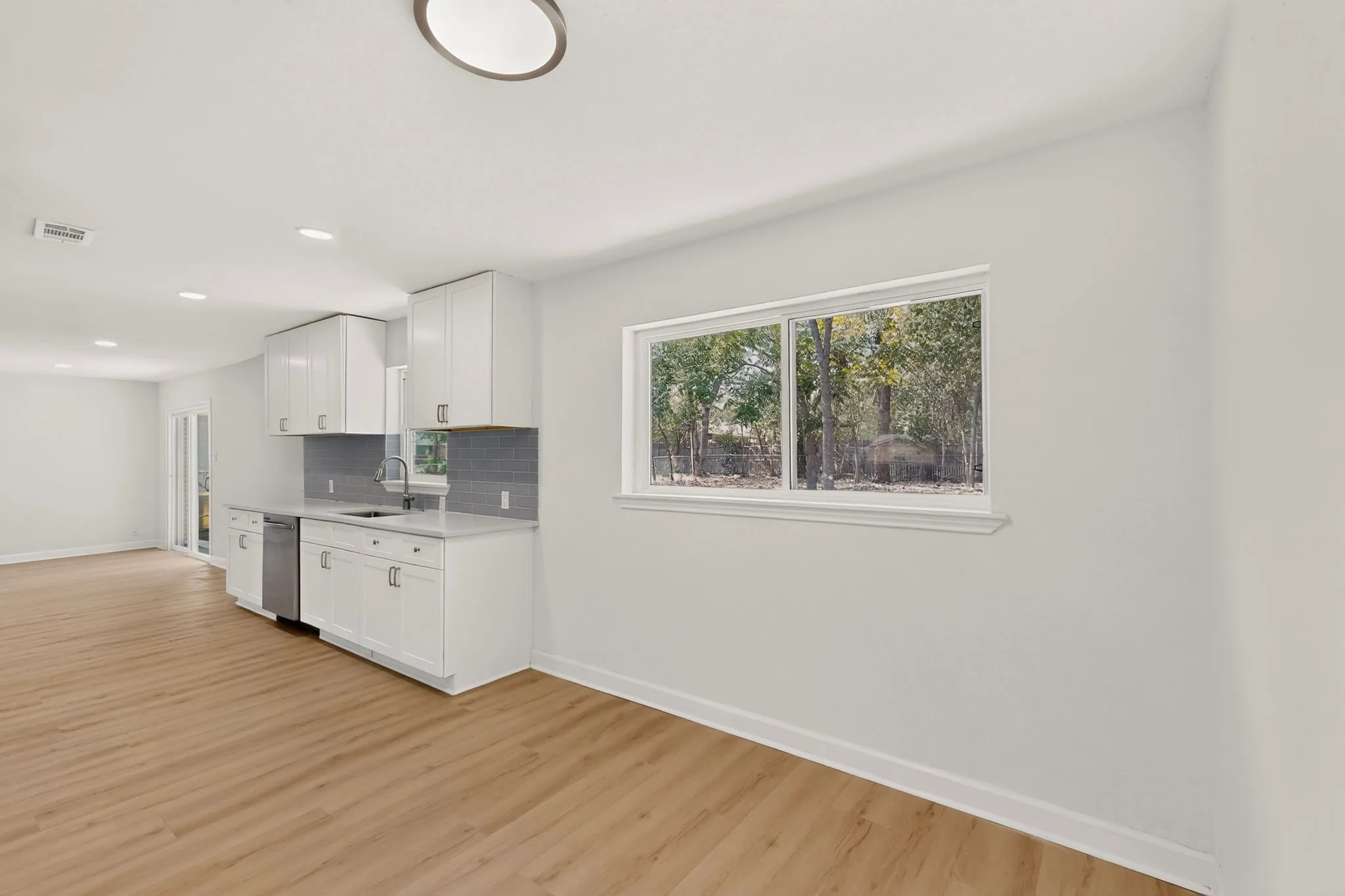 White cabinetry, stainless steel appliances, solid surface countertops, wood-finish flooring, and recessed lighting
