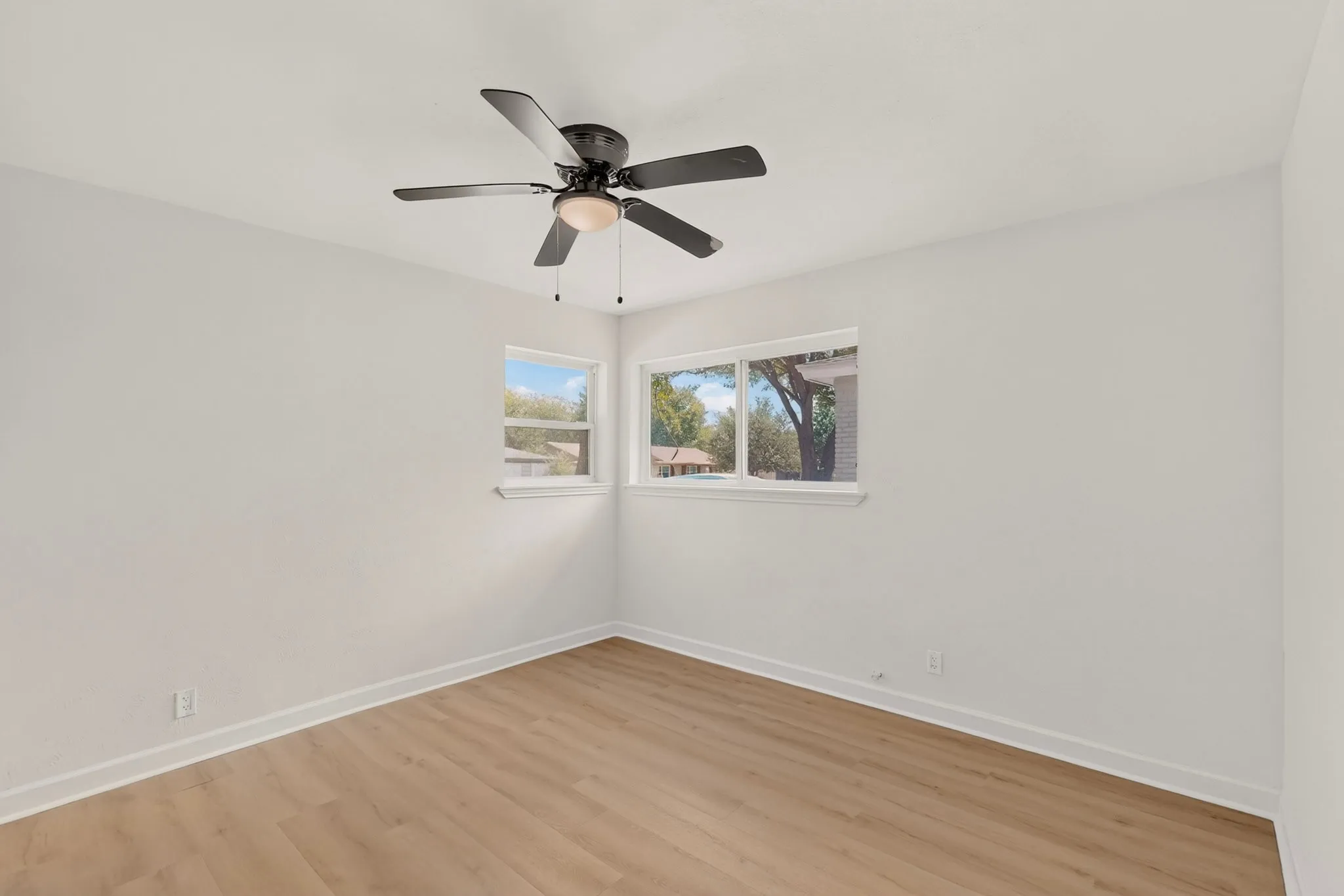 Wood-finish flooring, white walls, two windows, and a ceiling fan with integrated lighting
