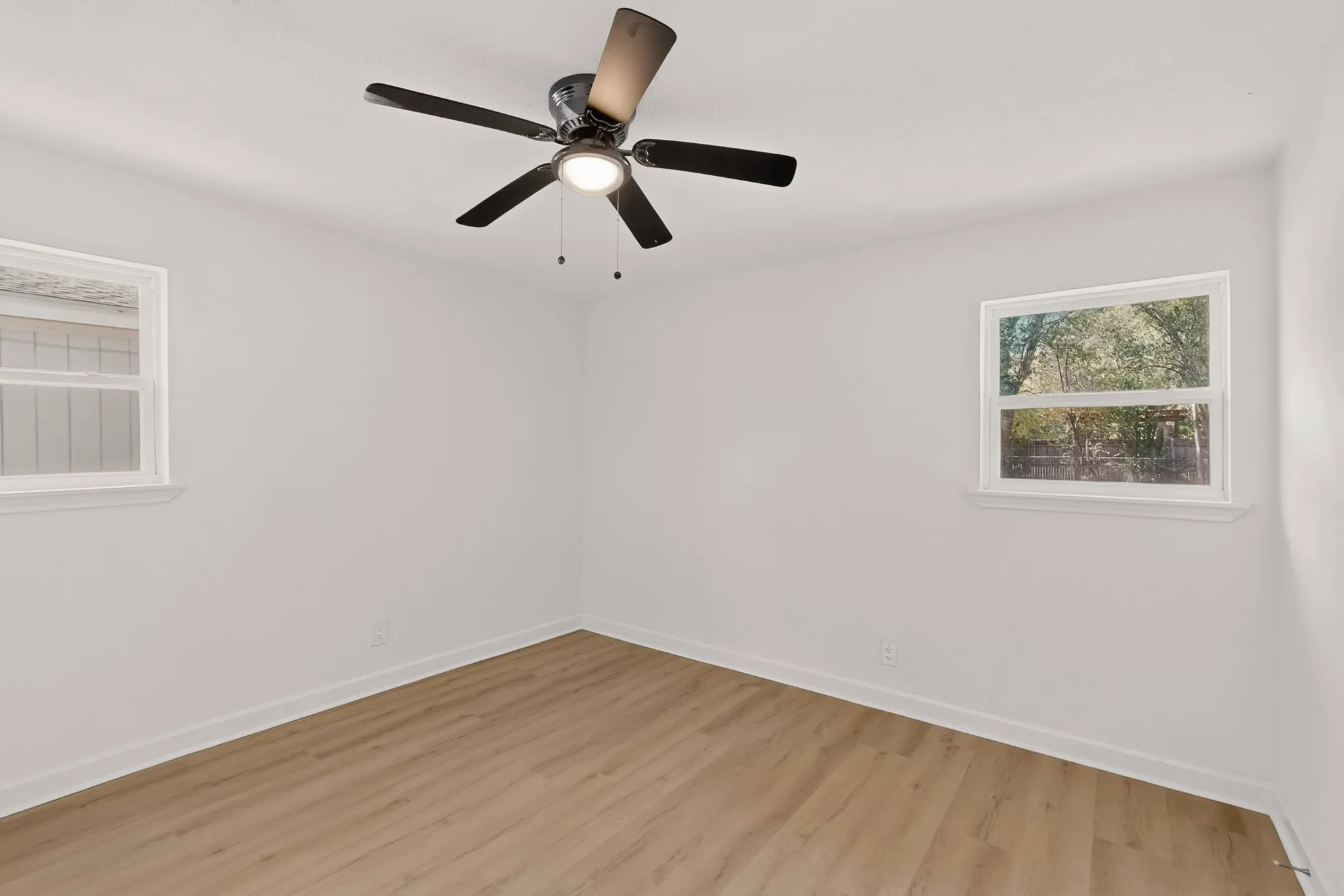 Wood-finish flooring, white walls, two windows, and a ceiling fan with integrated lighting