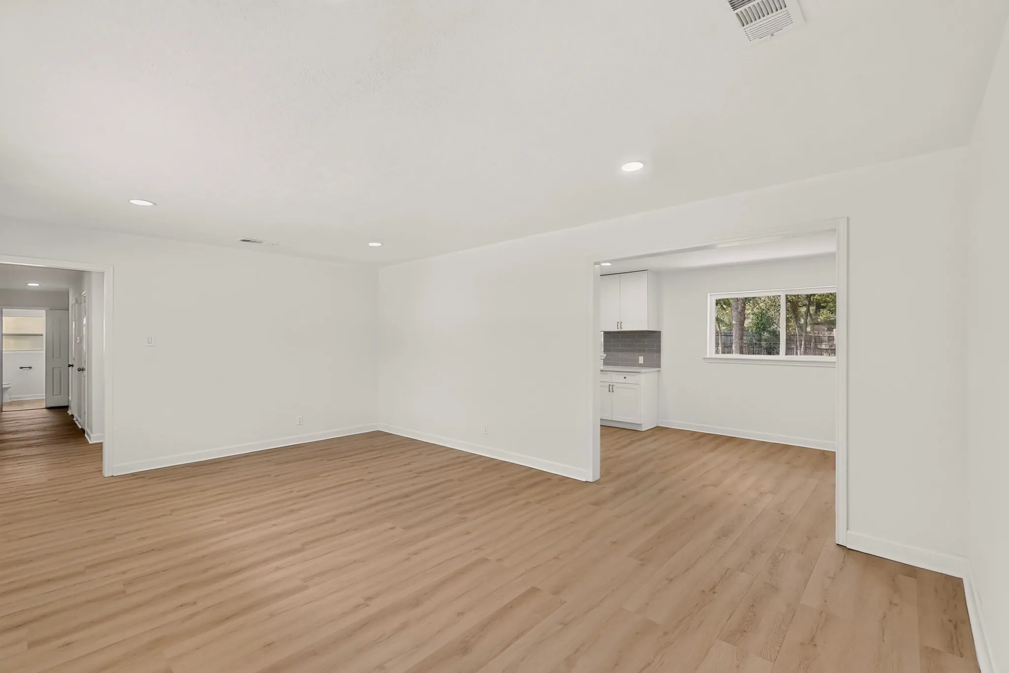 Recessed lighting, wood-finish flooring, white walls, kitchen cabinetry, and a window providing exterior views