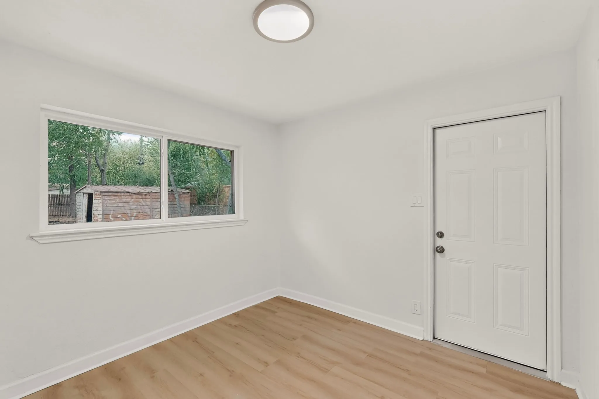 Recessed lighting, wood-finish flooring, white paneled door, and a white-trimmed window