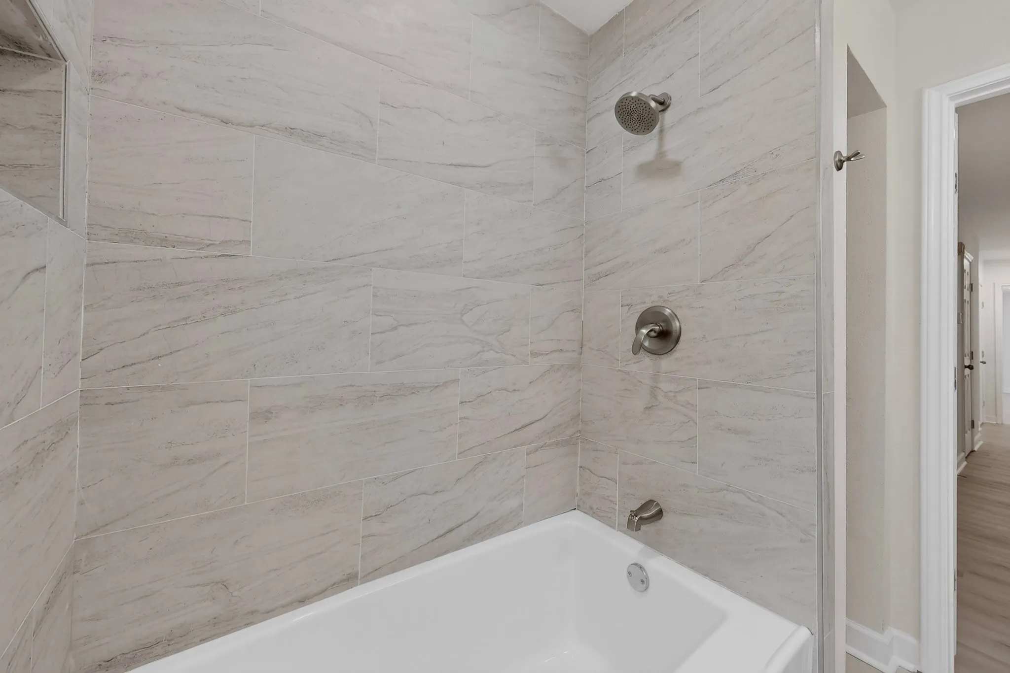 White porcelain bathtub with tile surround, brushed nickel fixtures, and integrated shower niche