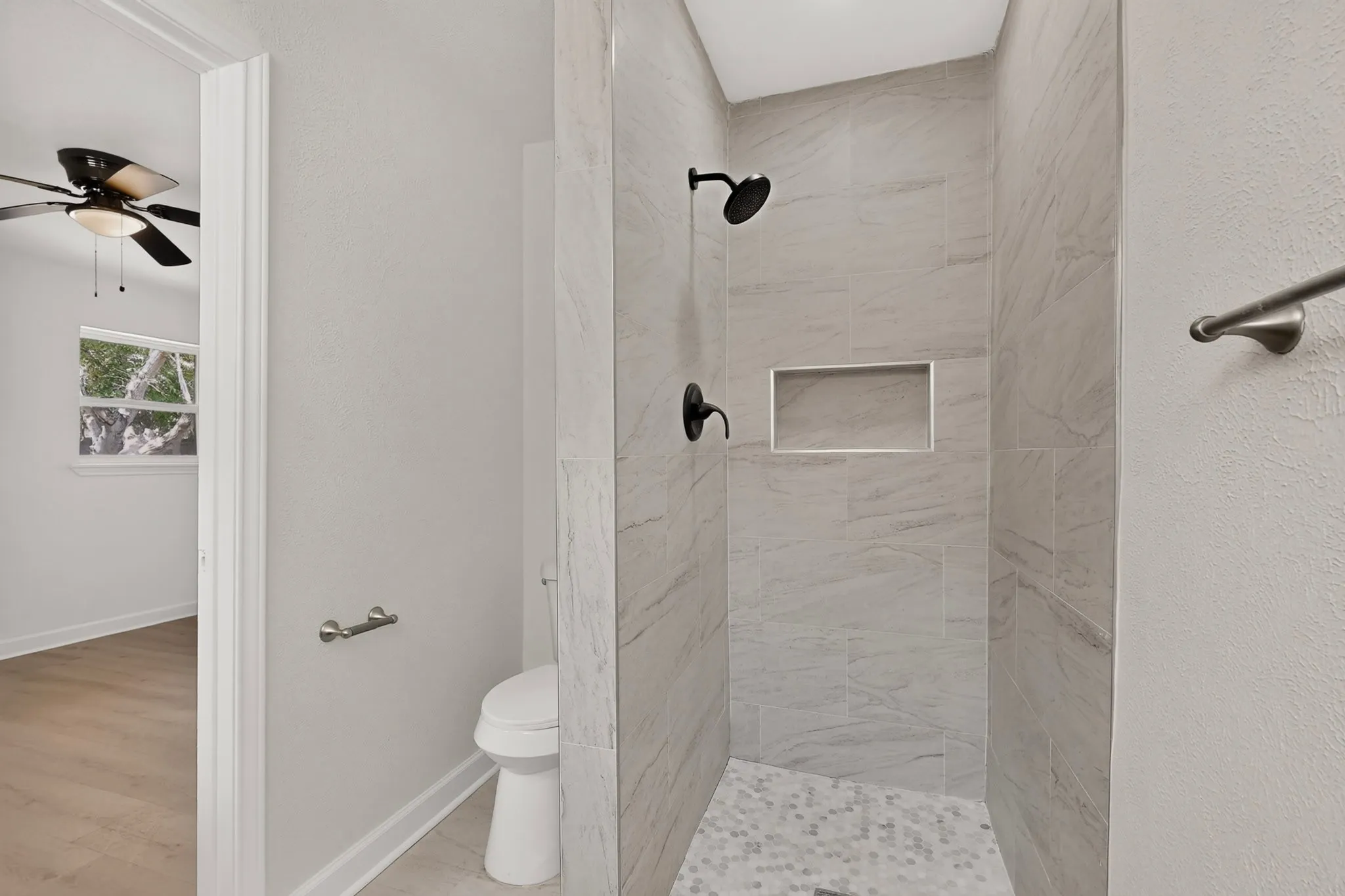 Walk-in shower with light-toned tiled walls, black-finish shower fixtures, and a recessed shower niche