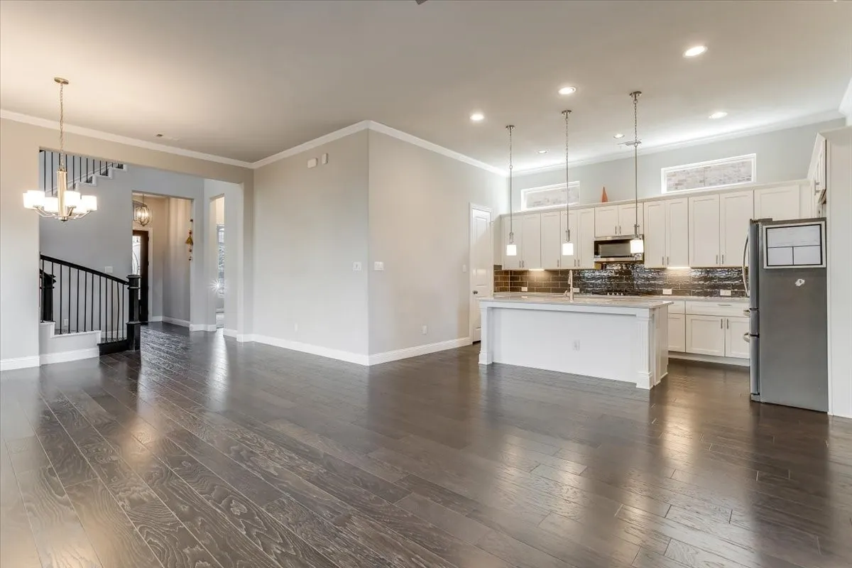 Wood-finish flooring throughout, kitchen with white cabinetry, stainless steel appliances, pendant lighting, and a kitchen island