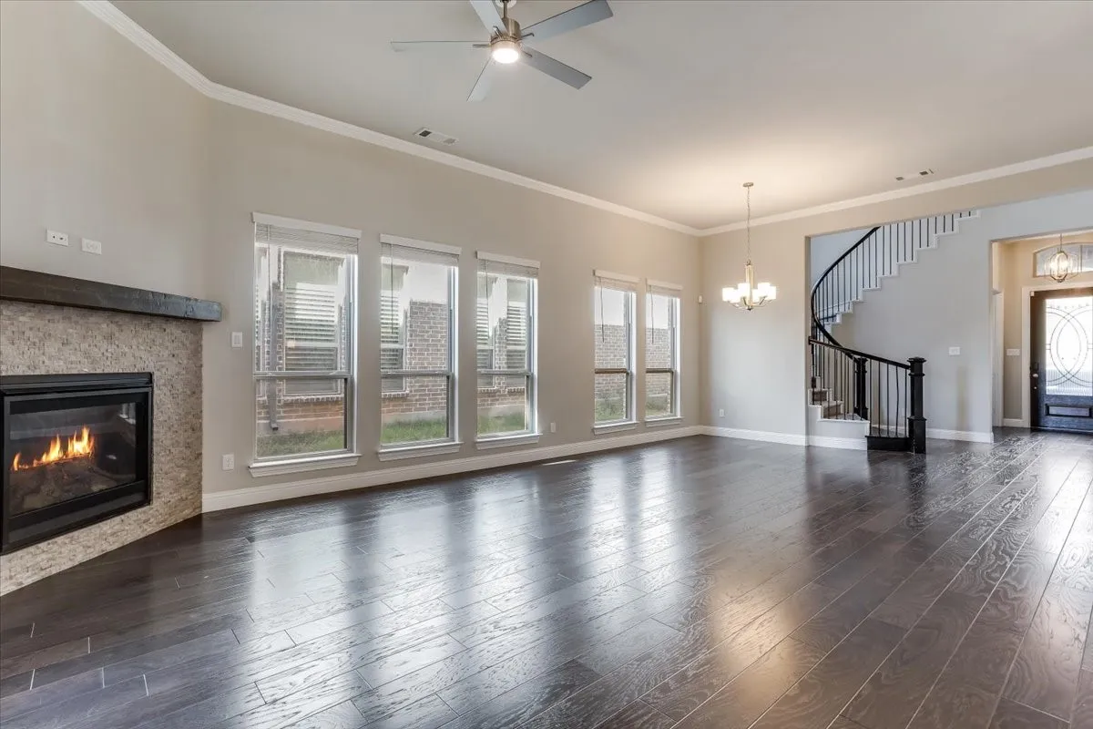 Spacious living area featuring dark wood-finish flooring, a contemporary ceiling fan, and a fireplace with a stone surround and wood mantle