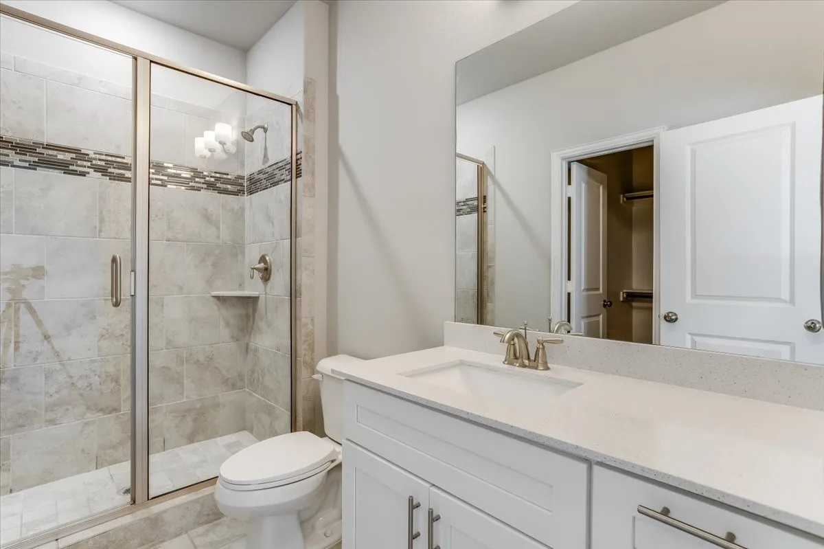 Glass-enclosed shower with tiled walls and a decorative mosaic band