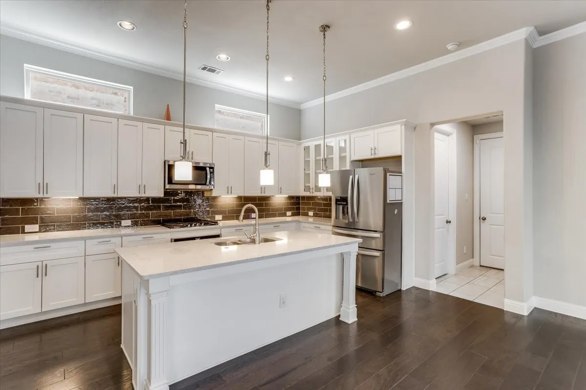 Kitchen featuring a central island with a sink, white cabinetry, integrated stainless steel appliances, and dark wood-finish flooring