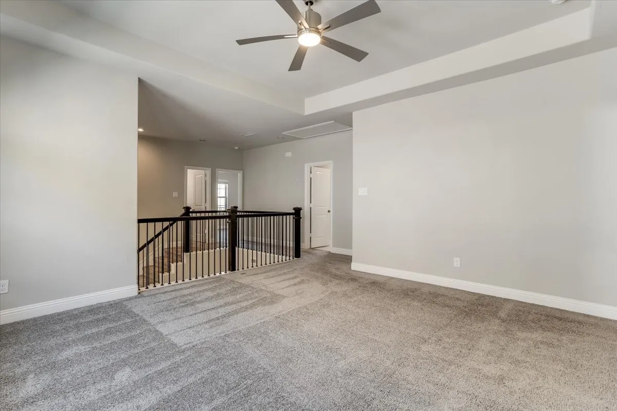 Spacious carpeted area with a ceiling fan, tray ceiling, and black spindle railing