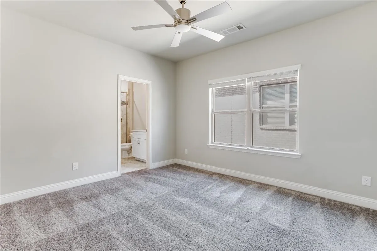 Neutral wall paint, ceiling fan, carpet flooring, window with blinds, and an adjoining bathroom