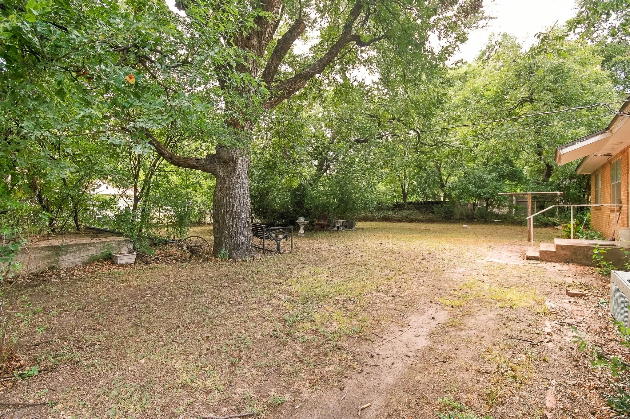 Expansive backyard featuring mature trees, a concrete patio, and a brick retaining wall