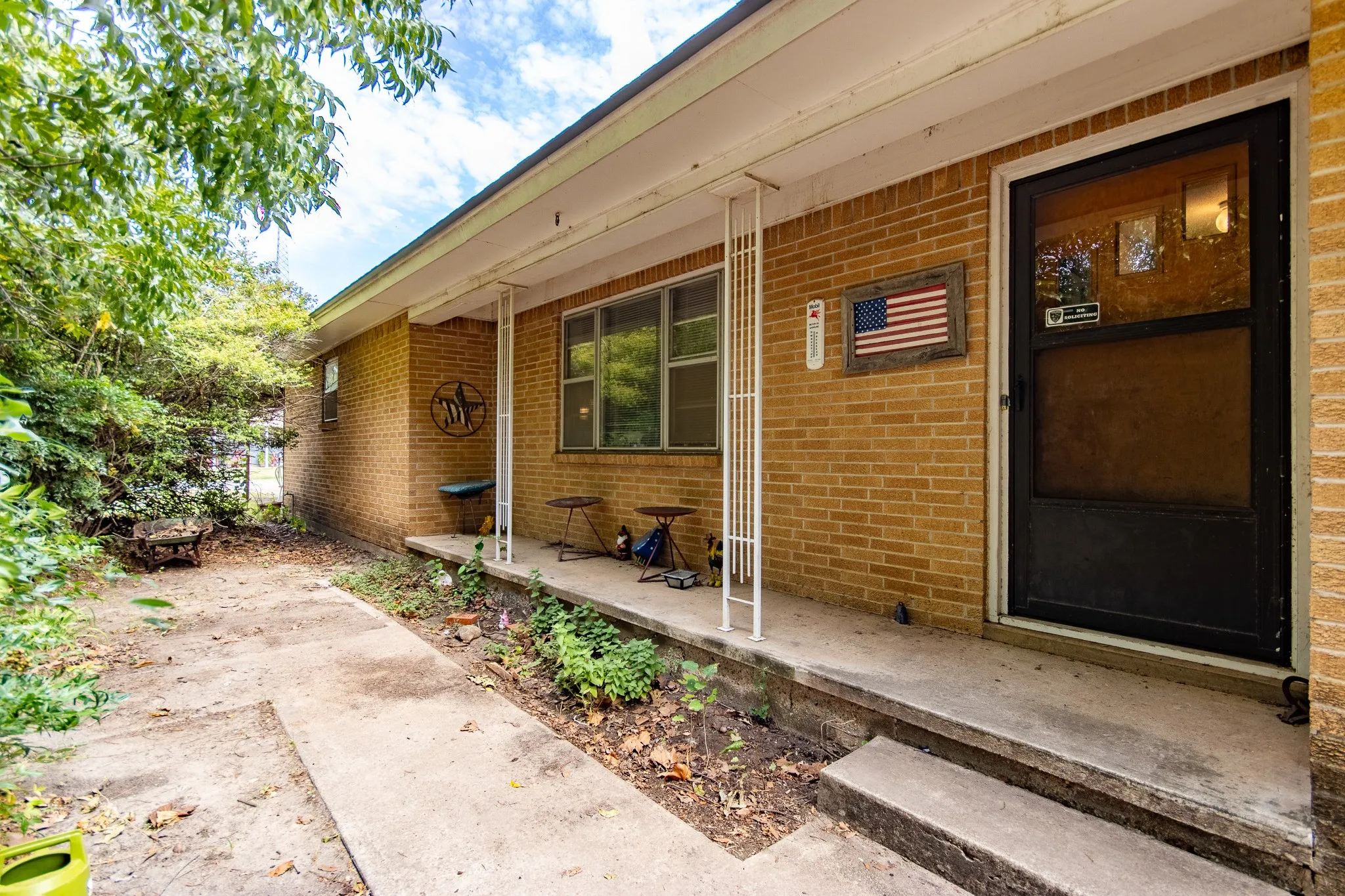 Brick exterior with covered front porch, concrete pathway, and mature trees