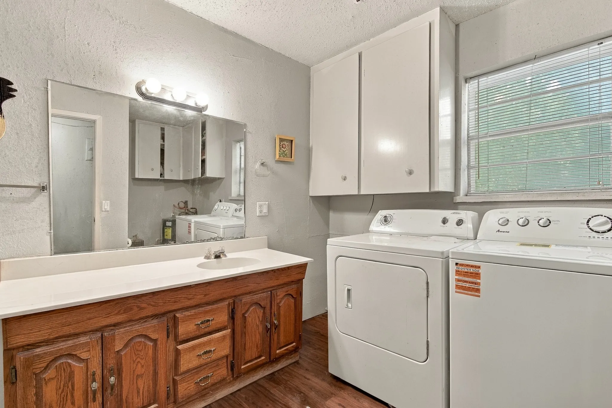 Laundry area with a built-in wood-finish vanity, integrated sink, and white overhead cabinetry