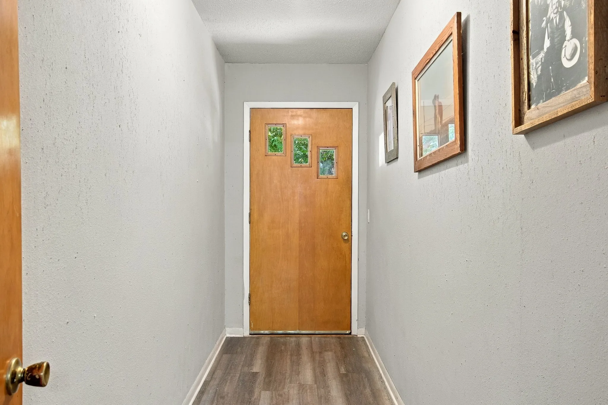Wood-finish flooring with light gray walls, leading to a wood-panel door with decorative glass inserts
