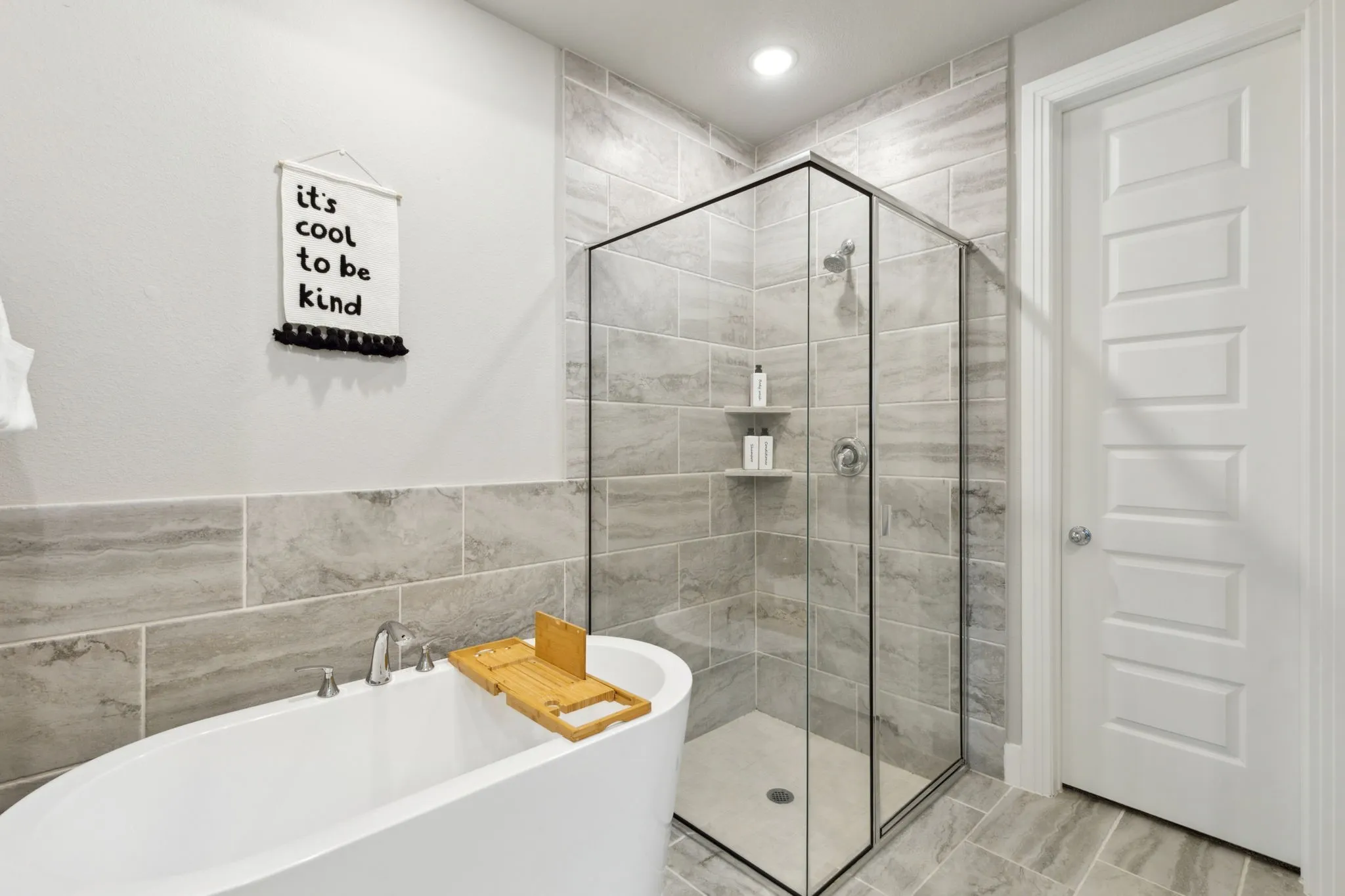 Freestanding bathtub with deck-mounted fixtures, glass-enclosed shower with built-in shelving, tiled shower surround, recessed lighting, and panel door