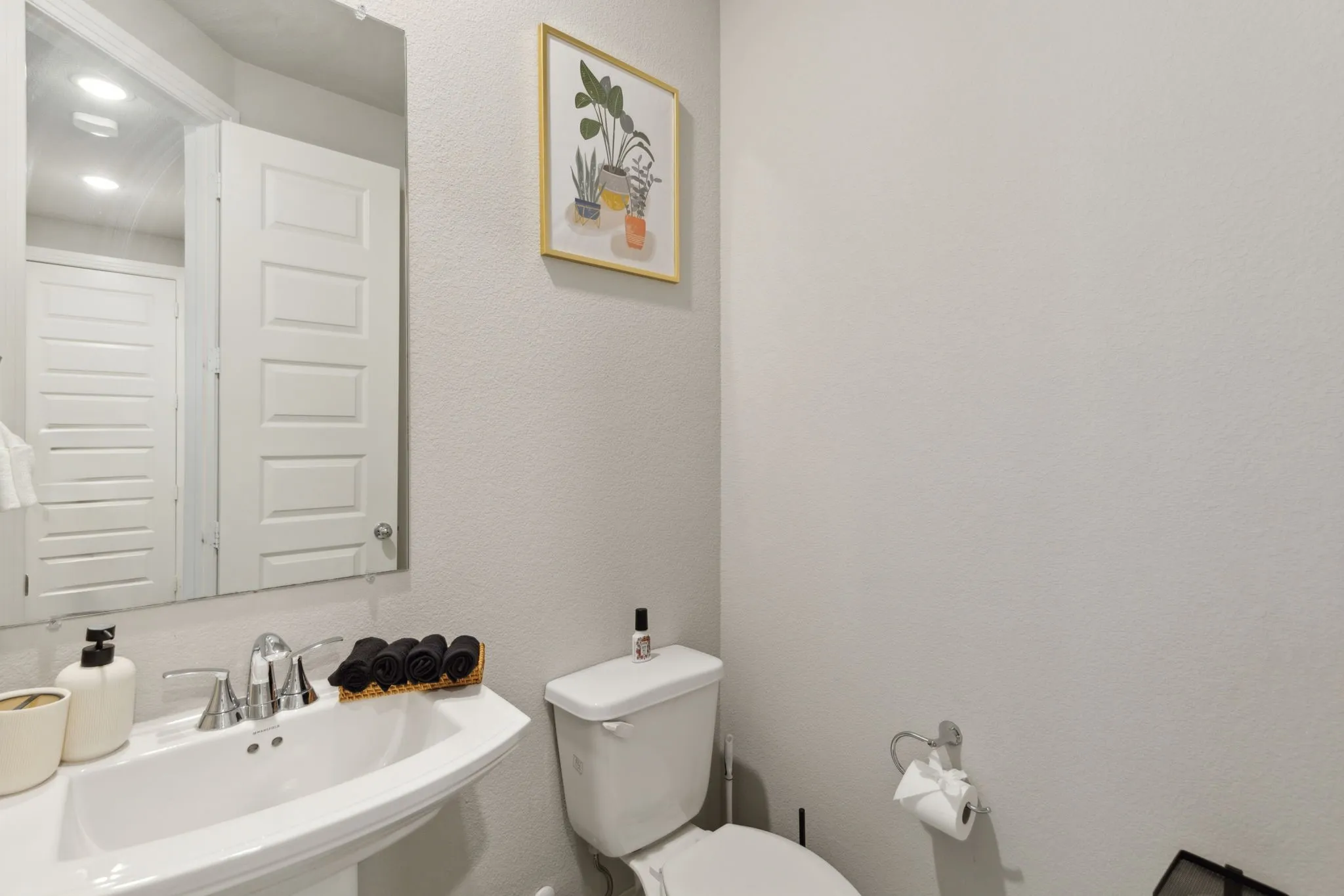 Pedestal sink with chrome-finish faucet, wall-mounted mirror, and paneled interior door