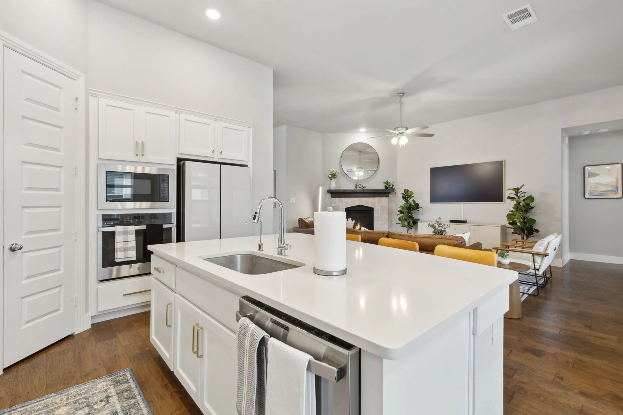 Kitchen island with integrated sink, stainless steel appliances, white cabinetry, and wood-finish flooring
