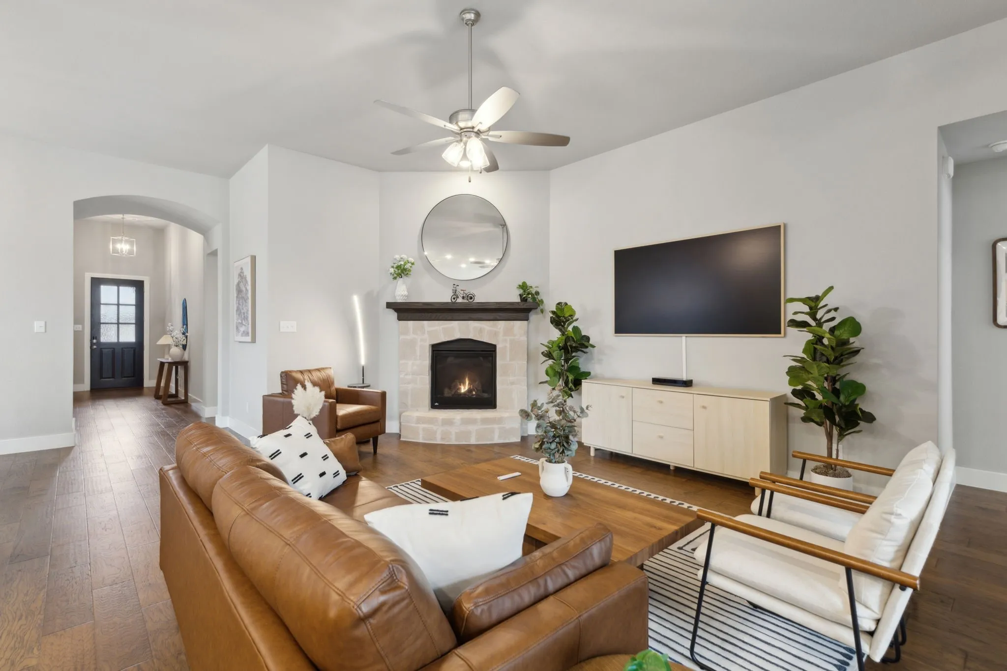 Living area featuring wood-finish flooring, a ceiling fan, and a stone-clad fireplace with a dark wood mantel