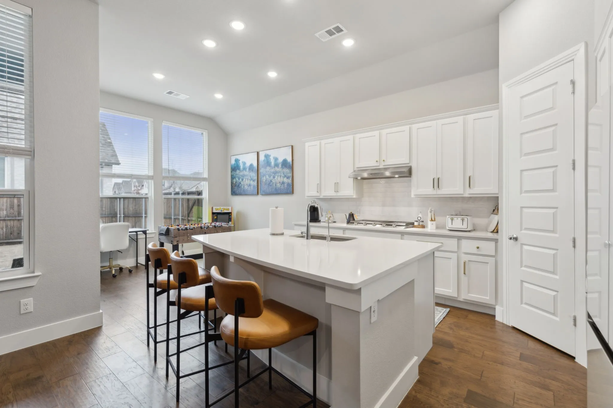 Kitchen featuring a large island with a solid surface countertop, white cabinetry with gold-toned hardware, stainless steel range hood, and wood-finish flooring