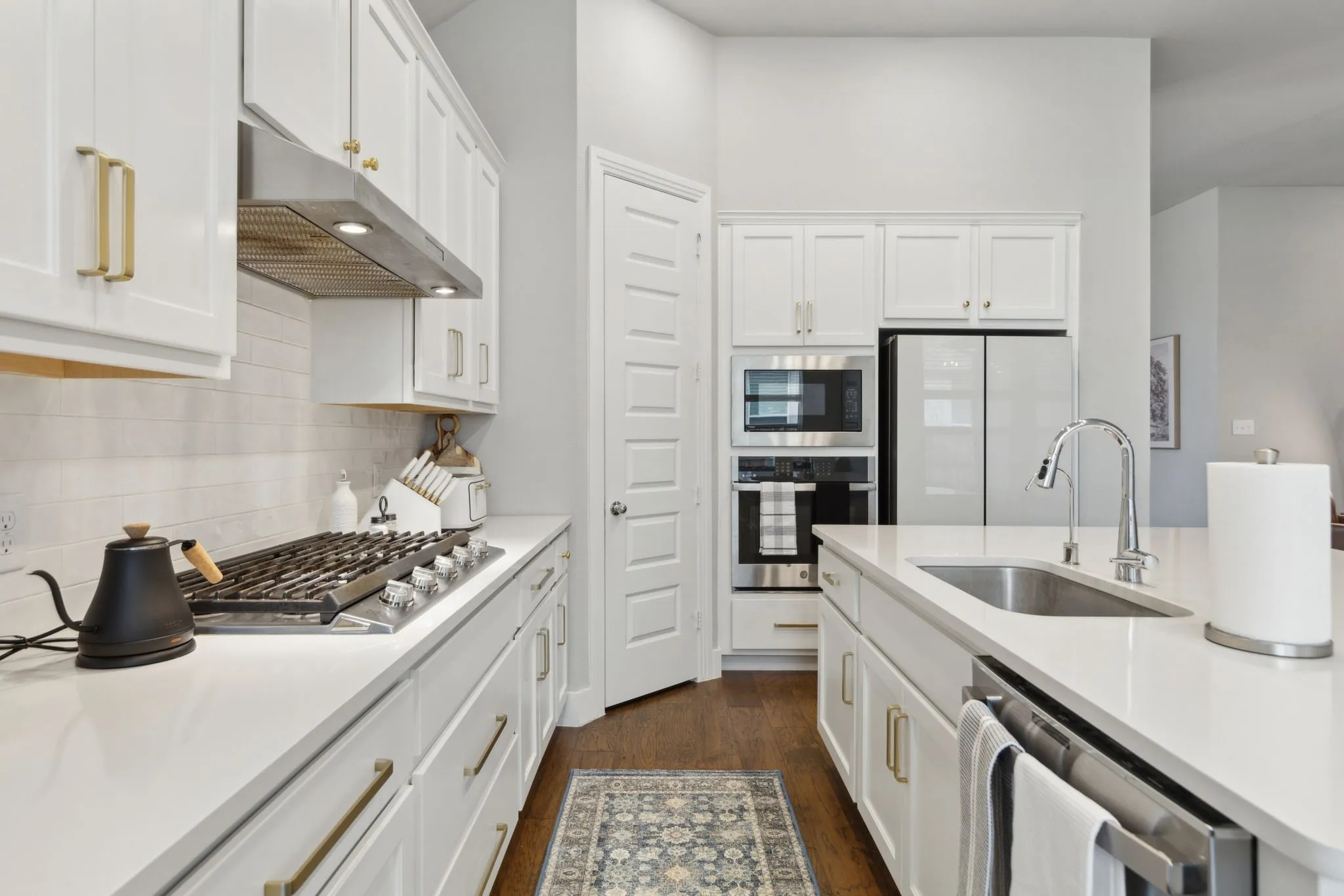 White cabinetry with gold-tone hardware, stainless steel appliances, white subway tile backsplash, and light-toned countertops