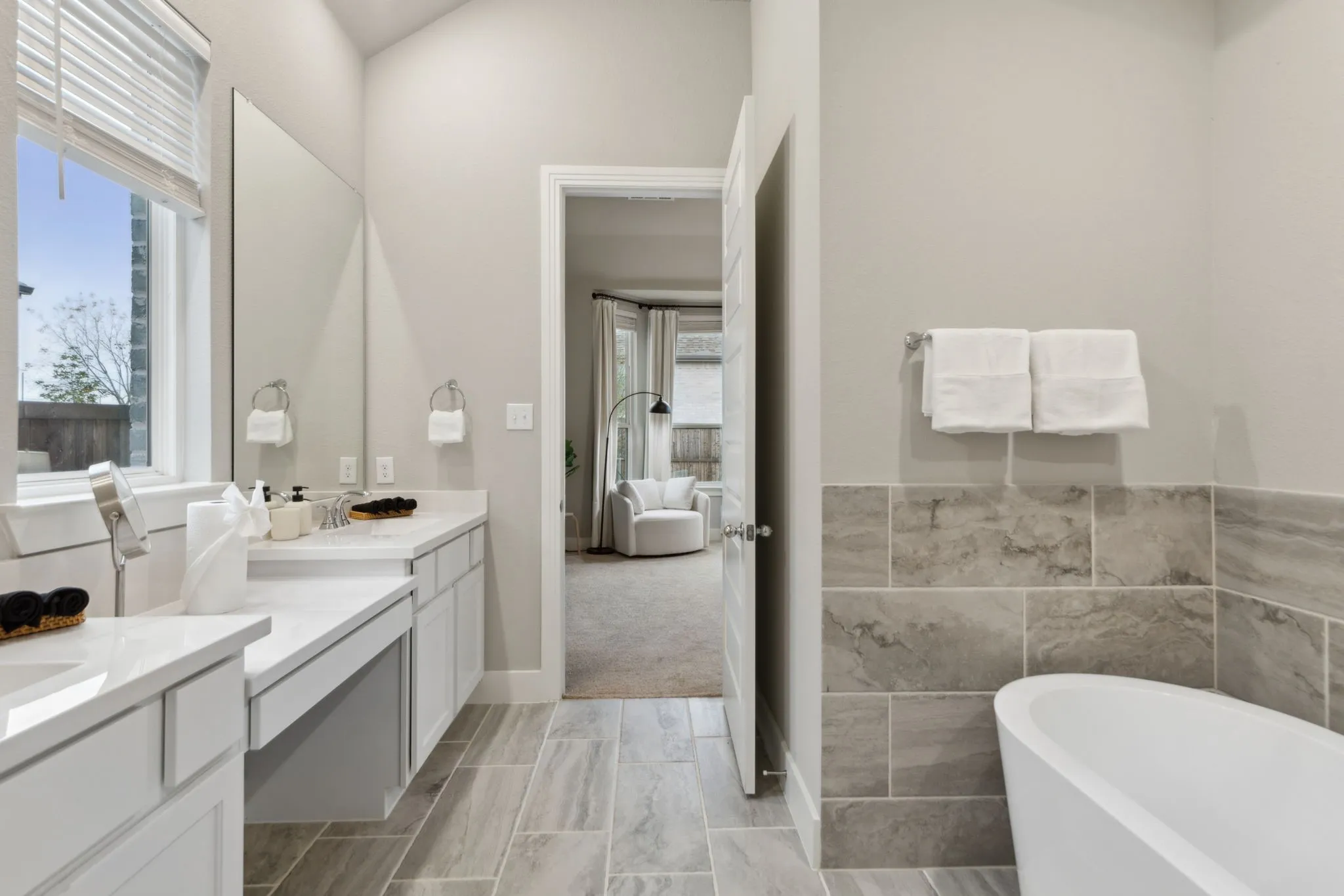 Dual vanity with white countertops, integrated makeup counter, freestanding tub, and tile-finish flooring