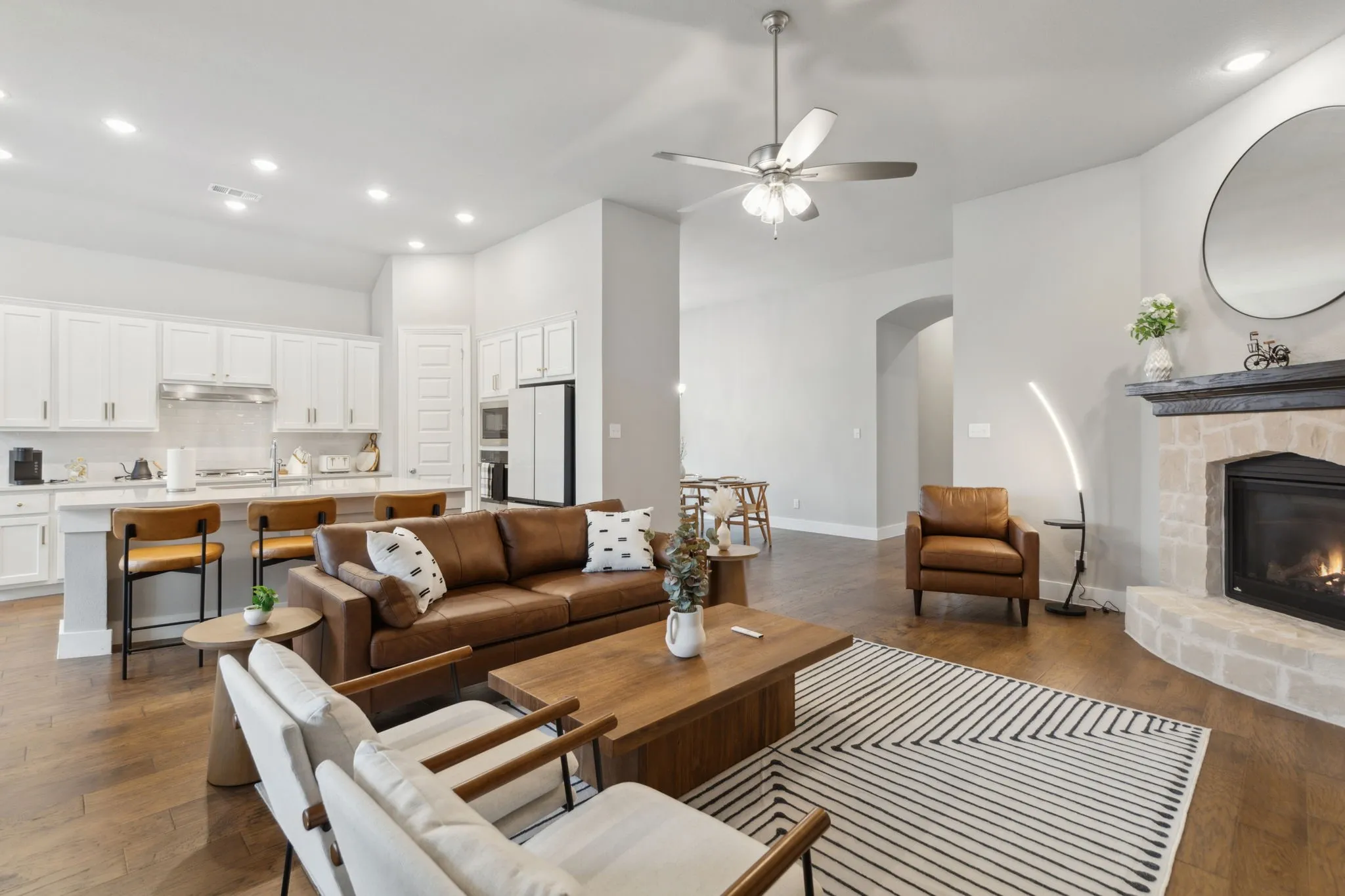Open concept living space featuring wood-finish flooring, a stone-surround fireplace, and a ceiling fan