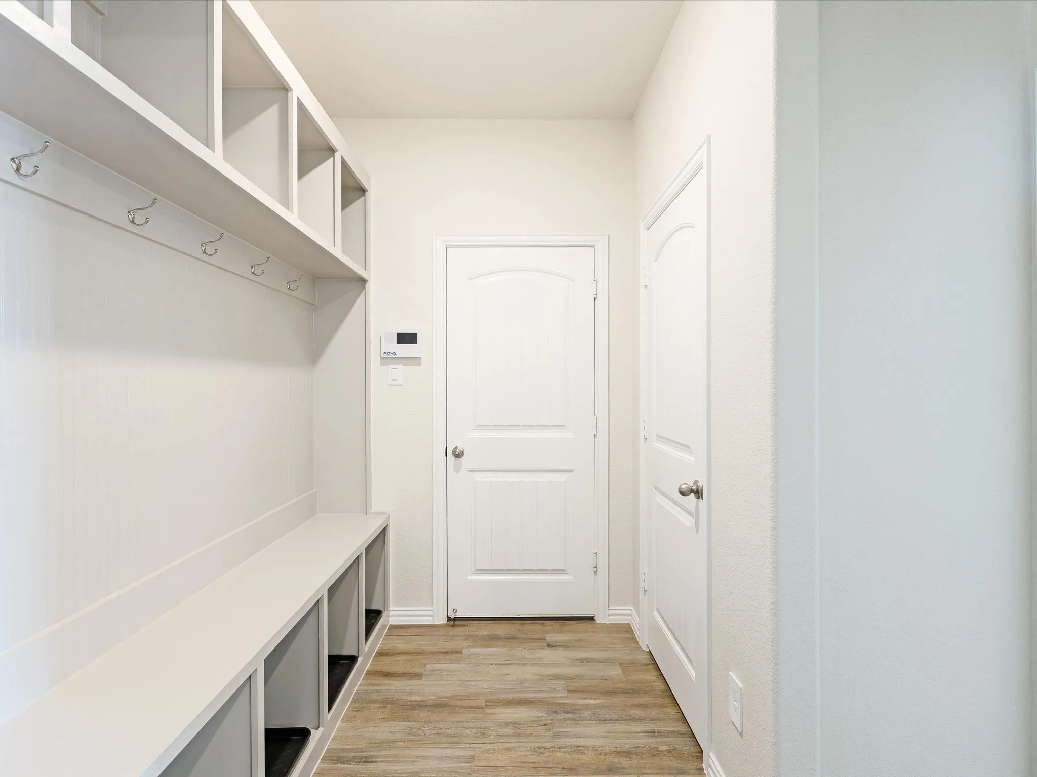 Built-in storage bench with cubbies, upper shelving, wall-mounted hooks, and wood-finish flooring