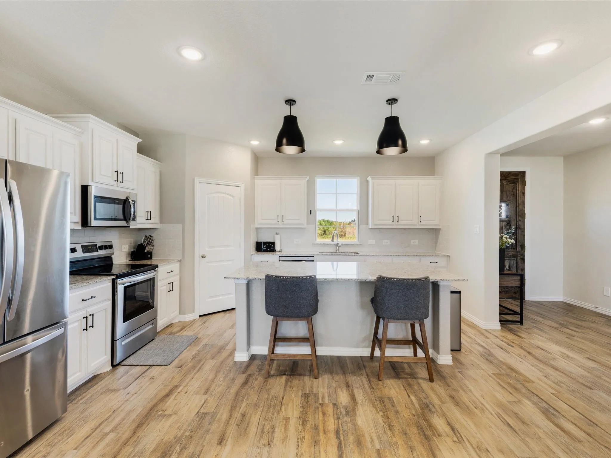 Kitchen featuring wood-finish flooring, white cabinetry, stainless steel appliances, a center island with a breakfast bar, and recessed lighting