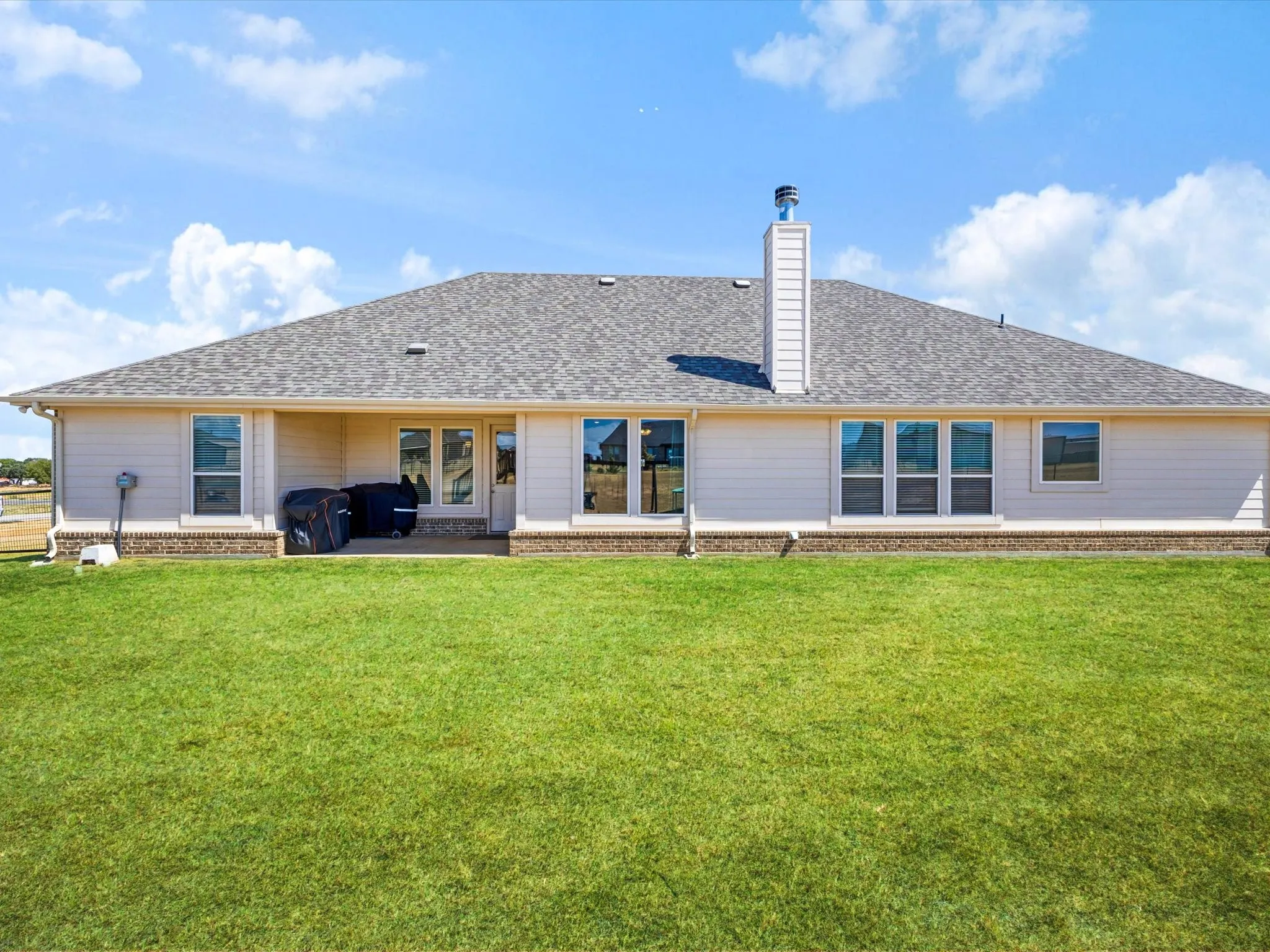 Expansive rear exterior with a covered patio, multiple windows, and a brick accent foundation