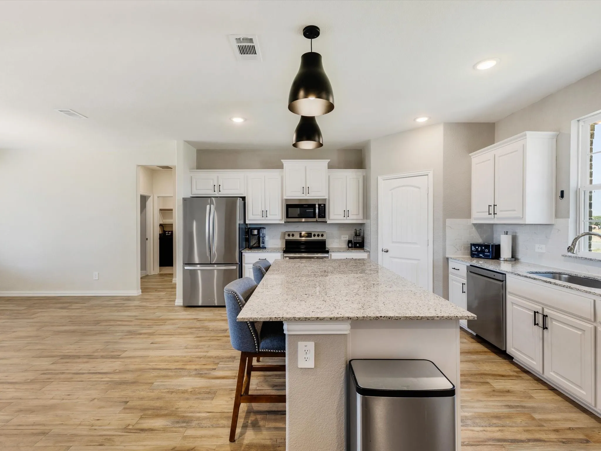 Kitchen featuring a large island with stone countertop, white cabinetry with dark hardware, stainless steel appliances, and wood-finish flooring