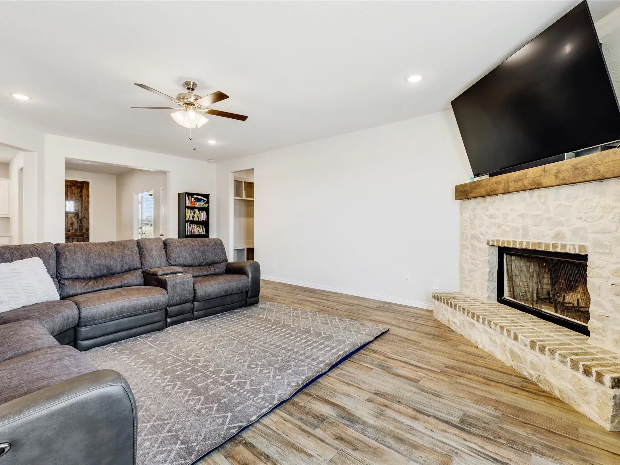 Stone-faced fireplace with a wood mantel, wood-finish flooring, recessed lighting, and a ceiling fan