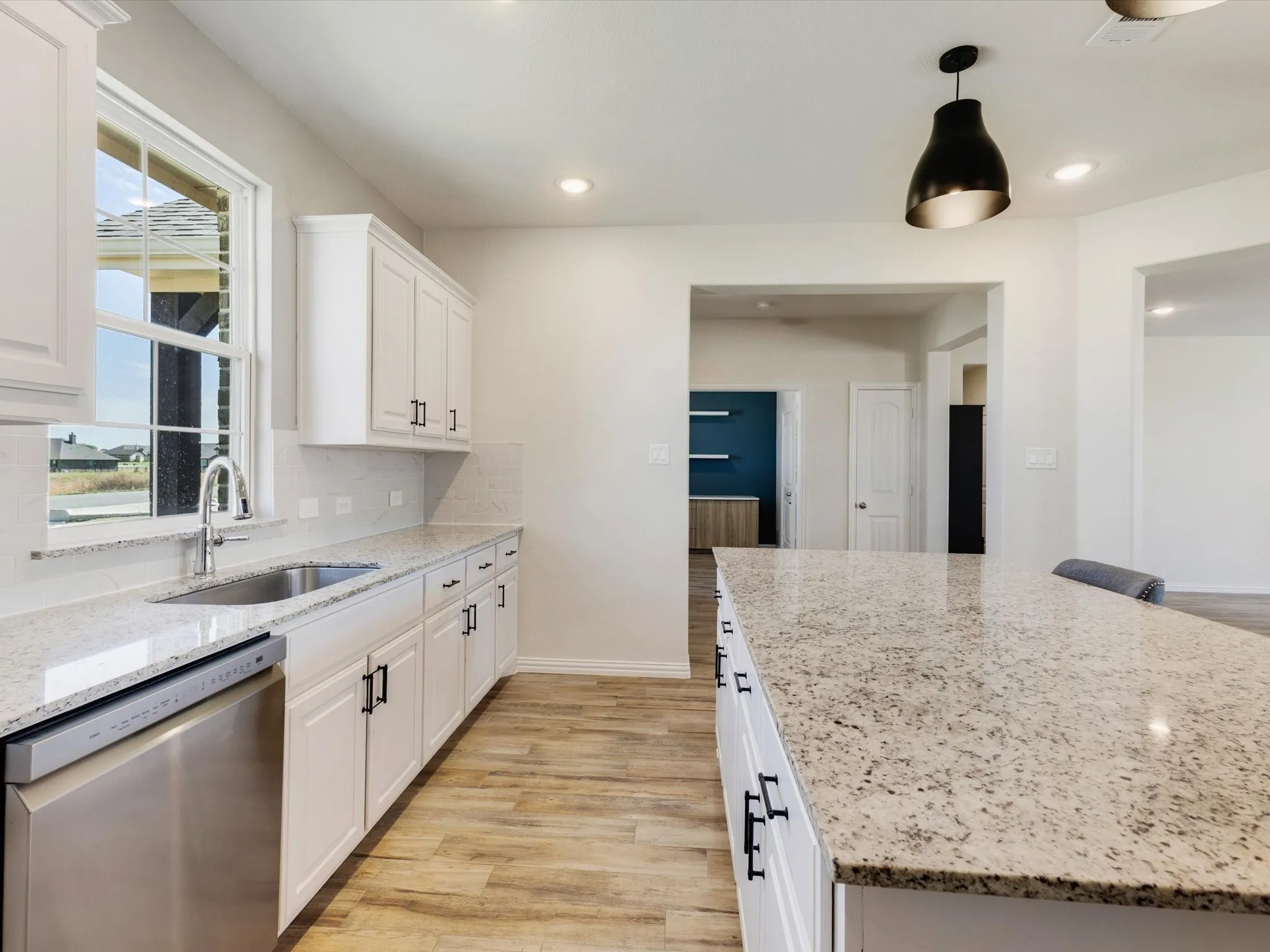 Kitchen featuring white cabinetry, light-colored countertops, stainless steel dishwasher, wood-finish flooring, and a window above the sink