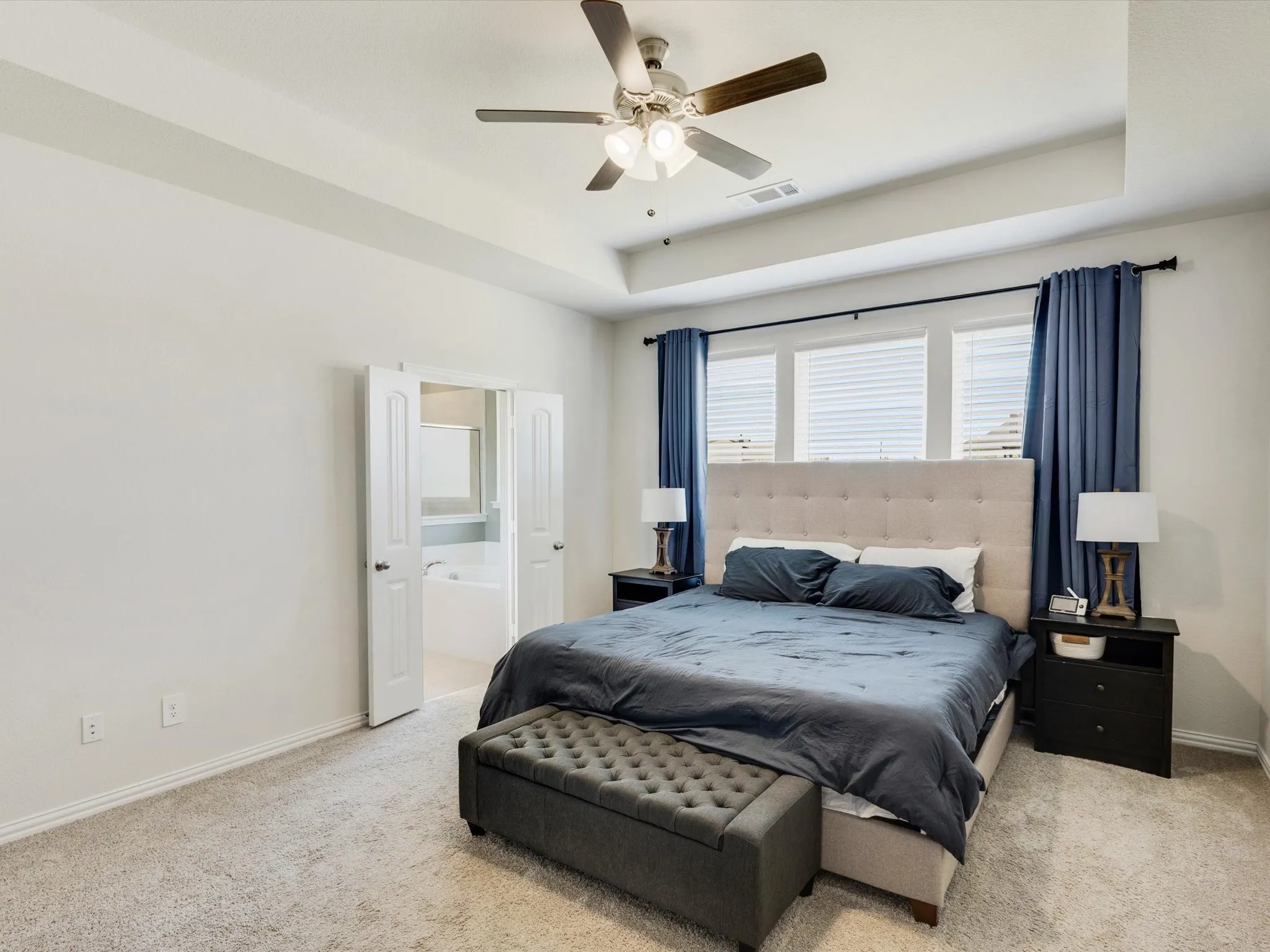 Carpeted bedroom featuring a tray ceiling, ceiling fan with integrated lighting, and multiple windows with blinds