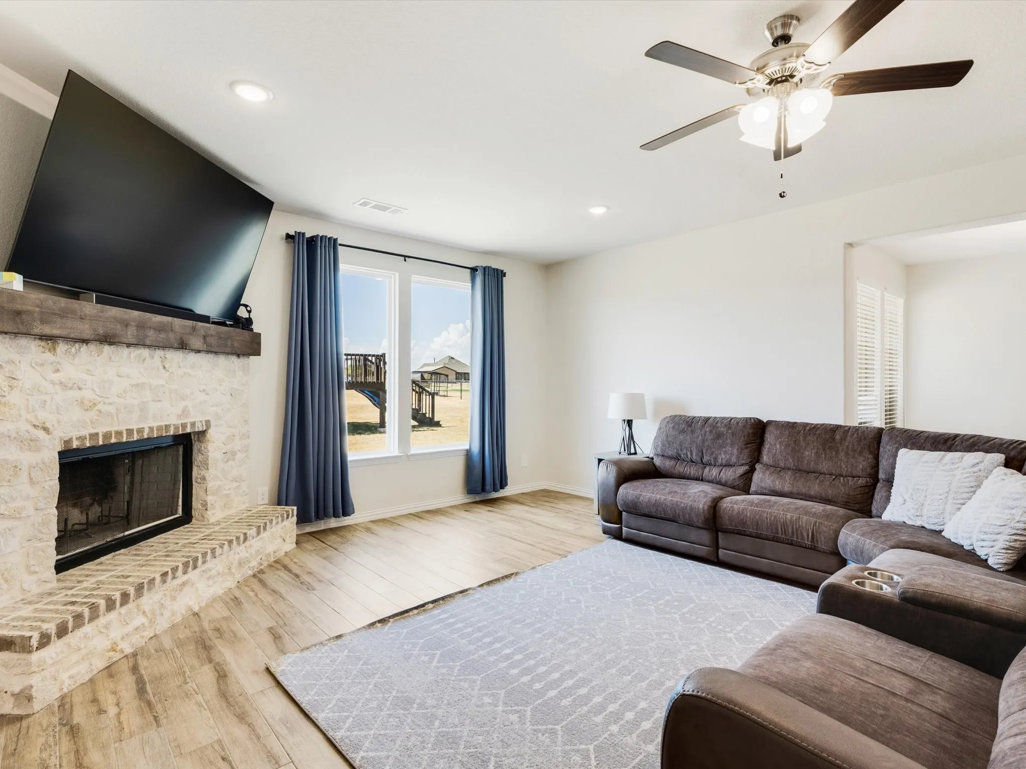 Living area featuring a stone fireplace with a wood mantle, wood-finish flooring, recessed lighting, a ceiling fan, and large windows