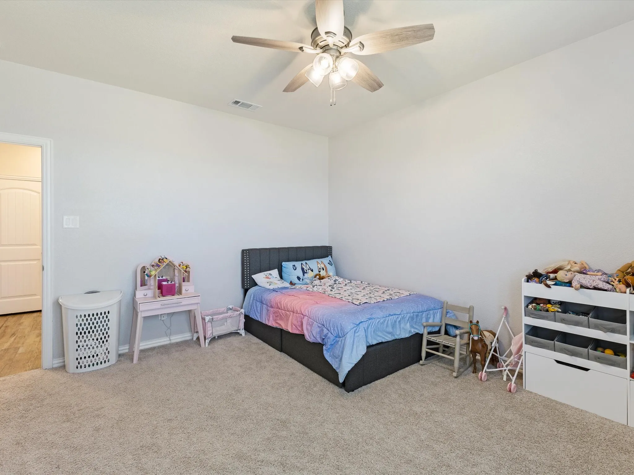 Textured carpeting, ceiling fan with integrated lighting, and a white paneled door