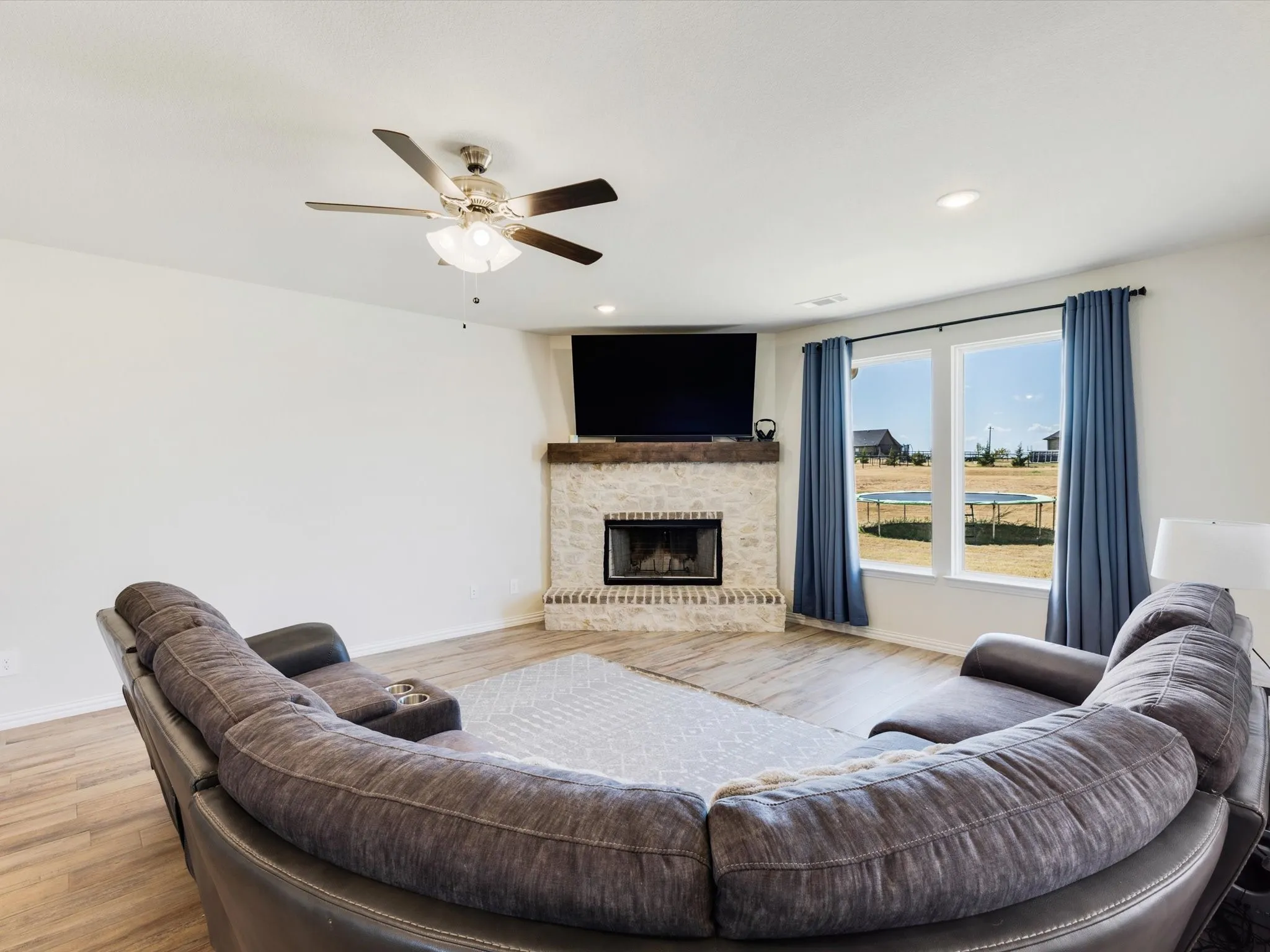 Stone-surround fireplace with a wood mantle, wood-finish flooring, recessed lighting, and a ceiling fan with light fixture