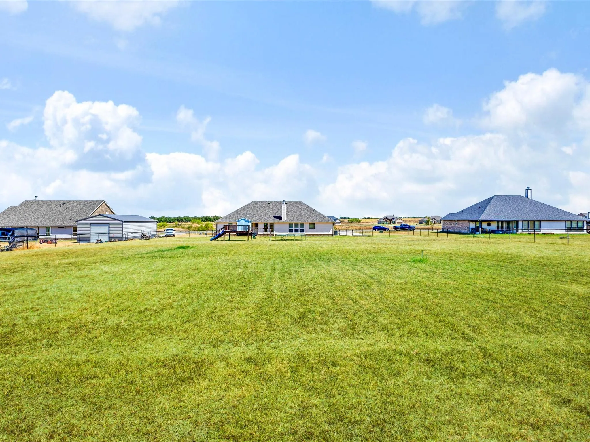 Expansive green lawn with a distant single-story residence and additional structure
