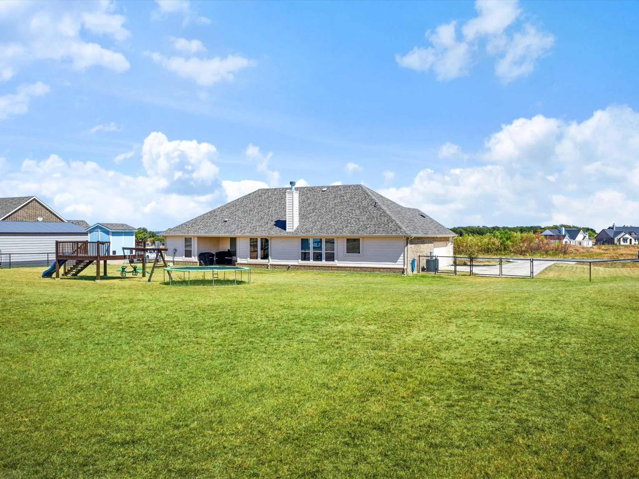 Expansive green space featuring a wood deck, multiple windows, and a single-story structure with a shingle roof and chimney
