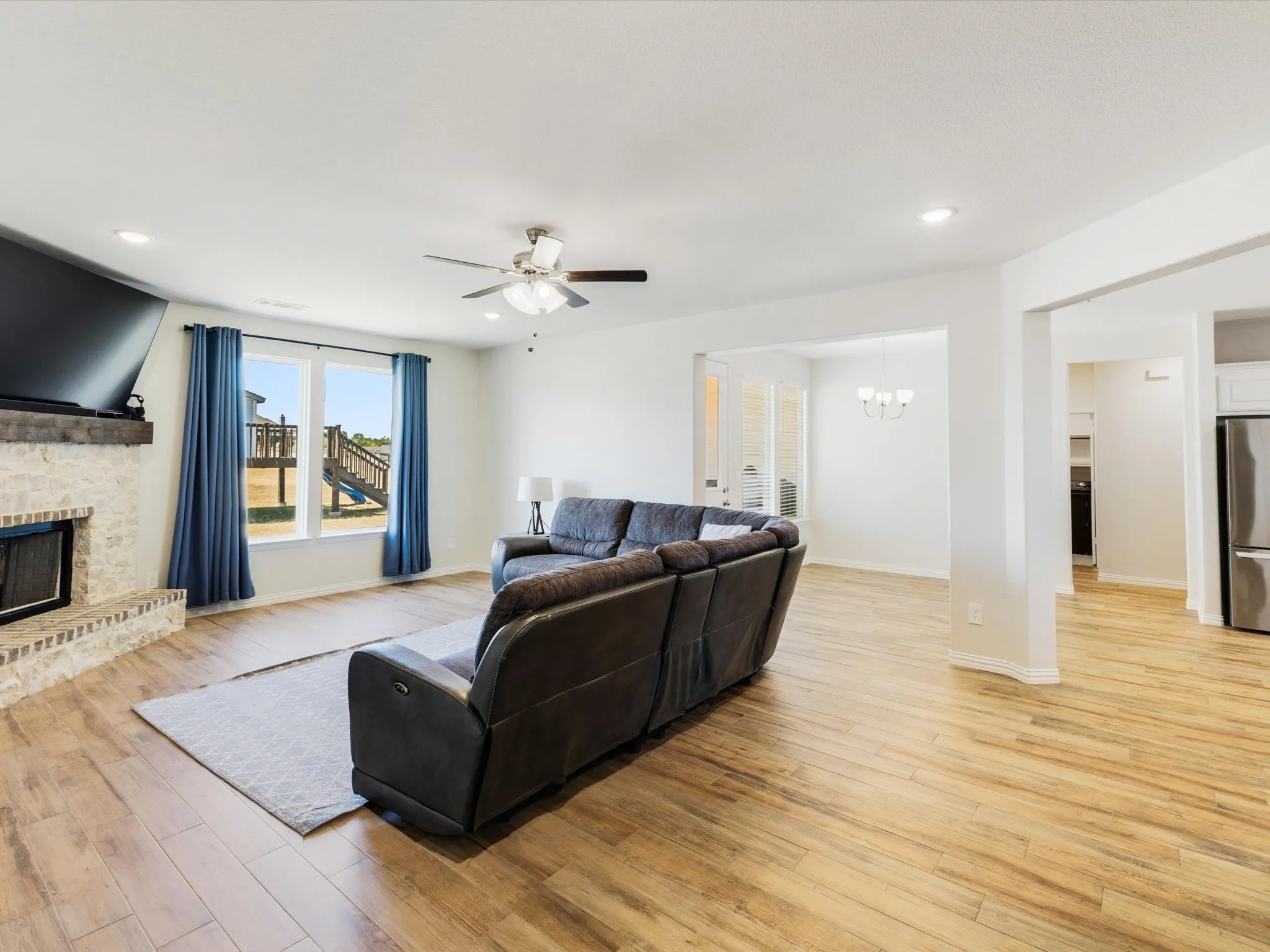 Expansive living space featuring wood-finish flooring, a stone fireplace with a substantial mantel, and recessed lighting