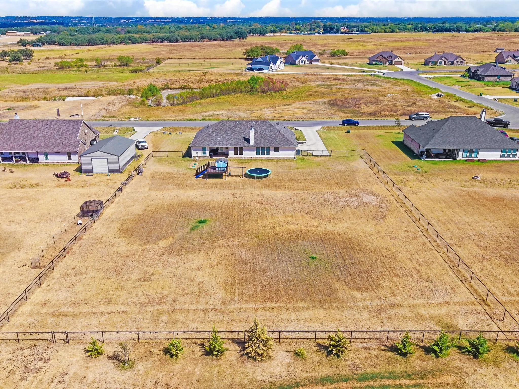 Expansive property featuring a fenced perimeter, a detached metal building, and a residential structure with a shingled roof